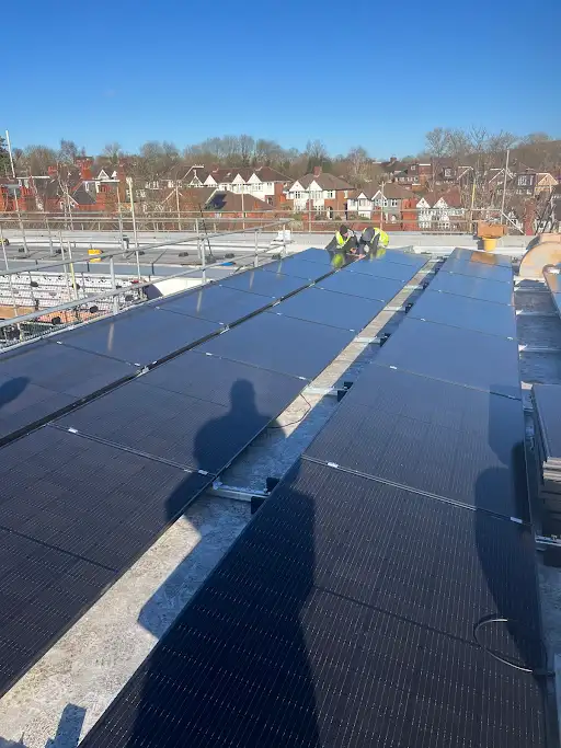 A man standing on top of a roof next to solar panels.